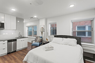 Open concept bedroom with white sheets, views of cityscape and ktichen