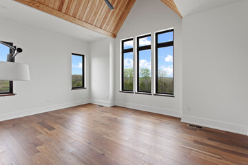 Large empty master bedroom with black windows and pitched wood ceiling