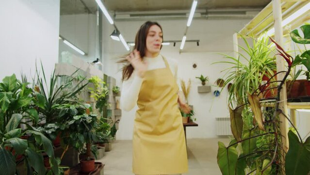 Florist woman dancing. Happy greenhouse worker listening to music, happy botanist having fun close-up, small business owner. Female gardener working in flower shop, plant store. 
