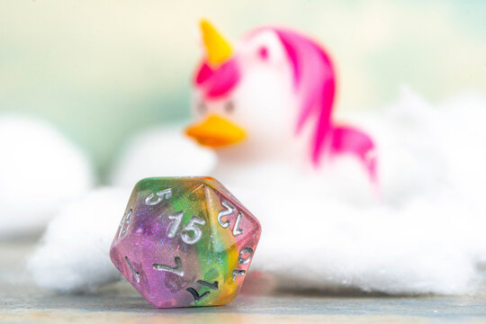Pastel rainbow D20 dice with unicorn duck in background
