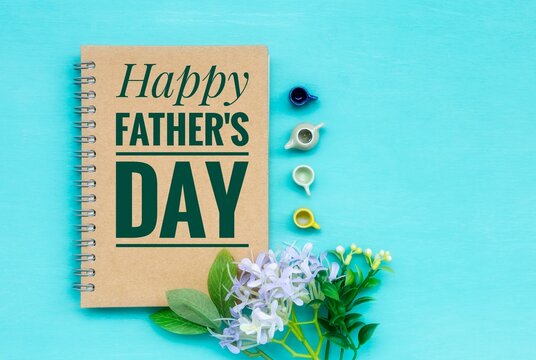 Happy Father's day banner on brown notebook cover with miniature tea cup and tea pot set with flower with space on blue background, greeting card idea