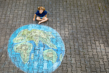Little preschool girl with earth globe painting with colorful chalks on ground. Positive toddler child. Happy earth day concept. Creation of children for saving world, environment and ecology.