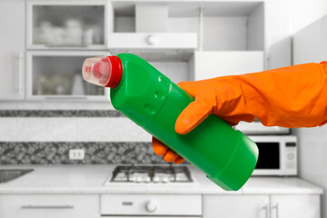 Woman's hand in protective glove with bottle of washing liquid.