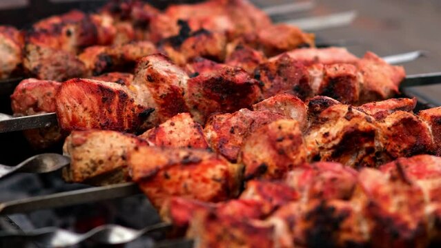 Close-up of grilling tasty dish on barbecue. Process of cooking yummy shashlik in nature. Delicious food on metal skewer in bbq. Time to picnic concept. Street food. Food festival. Pork at the stake