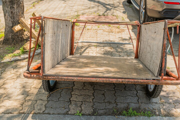 Two wheeled hand cart sitting in shade on brick sidewalk.