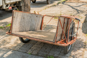 Two wheeled hand cart sitting in shade on brick sidewalk.