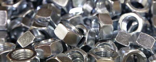 A lot of new gray nuts close up. Galvanized construction fasteners. Technical wide texture for background.