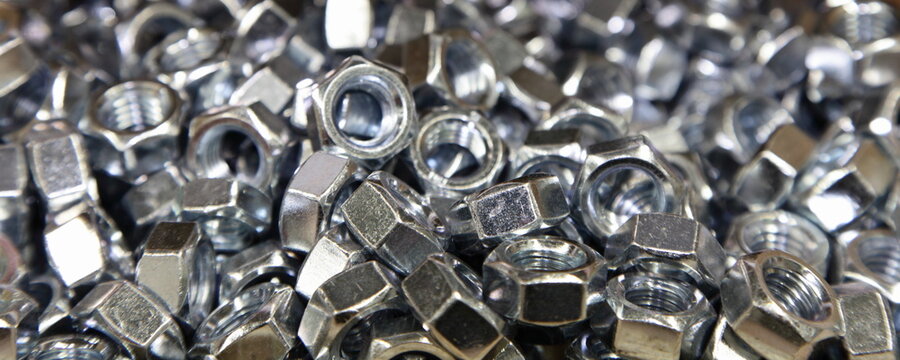 A many new gray shiny nuts closeup wide view. Galvanized construction fasteners. Technical texture for the background.