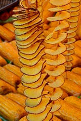long skewers of fried potato chips with peel and yellow organic corn cobs with  for sale in street food stall