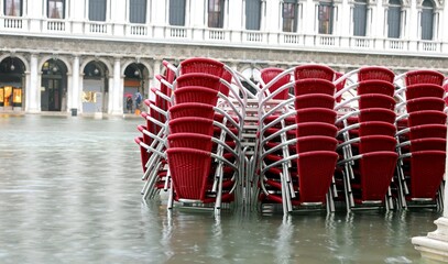 red chairs of the outdoor bar in the flooded Square of Saint Mark during tide in Venice in Italy in...