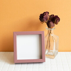 Blank picture frame and red dry rose on white table. orange wall background. copy space