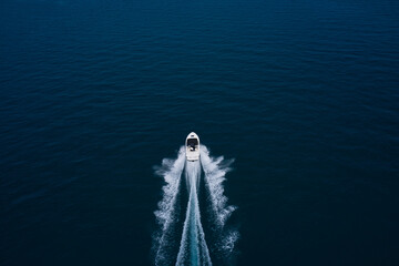 Drone view of a boat sailing. Top view of a white boat sailing to the blue sea. Motor boat in the sea. Travel - image. Large white boat fast movement on blue water aerial view.