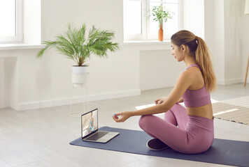 Calm relaxed young woman woman doing yoga looking tutorial on yoga classes on laptop. Woman in...