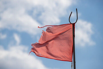 Red torn old flag on the sea against the blue sky.