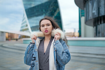 Fototapeta premium A fashionable girl with a wavy hairstyle and red lips poses on the street. Brunette in a jacket and a black skirt look away to the street ..