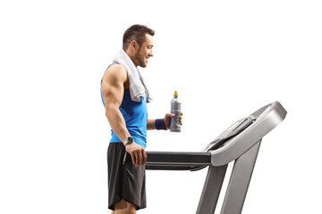 Young man standing on a treadmill with a bottle of isotonic drink