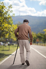 Elderly man walking with a cane on an asphalt pedestrian lane