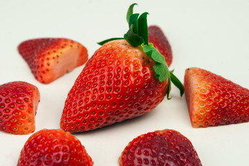 
whole strawberry in the foreground with a split strawberry on a white background
