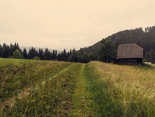 Autumn view of the valley and wooden cottages below the dark and foggy mountains.
