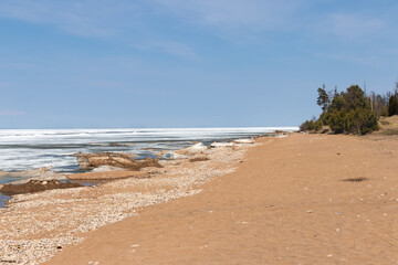 The coast of Lake Baikal, landscape with a sandy beach and an icy edge of the lake on a sunny spring day