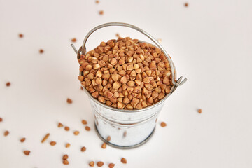 Miniature metal bucket filled with buckwheat on a white background.