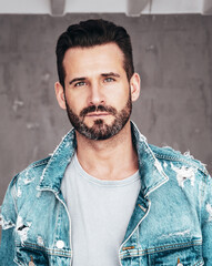 Closeup portrait of handsome confident stylish hipster lambersexual model. Sexy man dressed in jeans jacket. Fashion male posing on grey background in studio