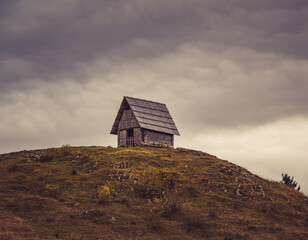 Autumn view of the valley and wooden cottages below the dark and foggy mountains.