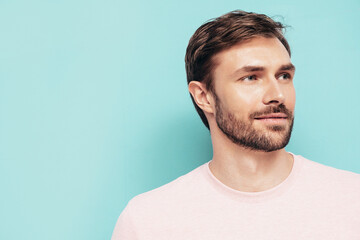 Fototapeta premium Closeup portrait of handsome smiling stylish hipster lambersexual model. Sexy man dressed in pink T-shirt and trousers. Fashion male isolated on blue wall in studio