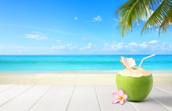 Coconut  juice on wooden table with beach and blue sky background.