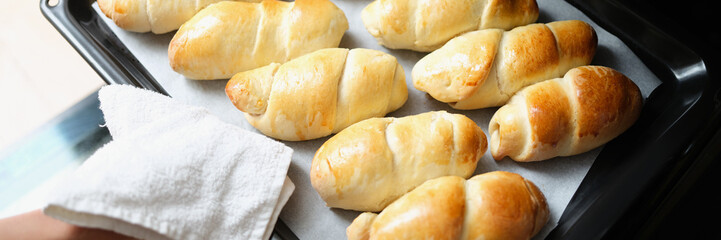 A woman takes buns out of the oven on a baking sheet