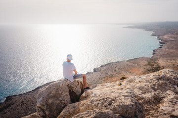Fototapeta na wymiar Summer landscape in Cyprus. View from the top of Cape Greco. Morning sunrise in Cyprus. A man sitting on the edge of a cliff and admires the scenery