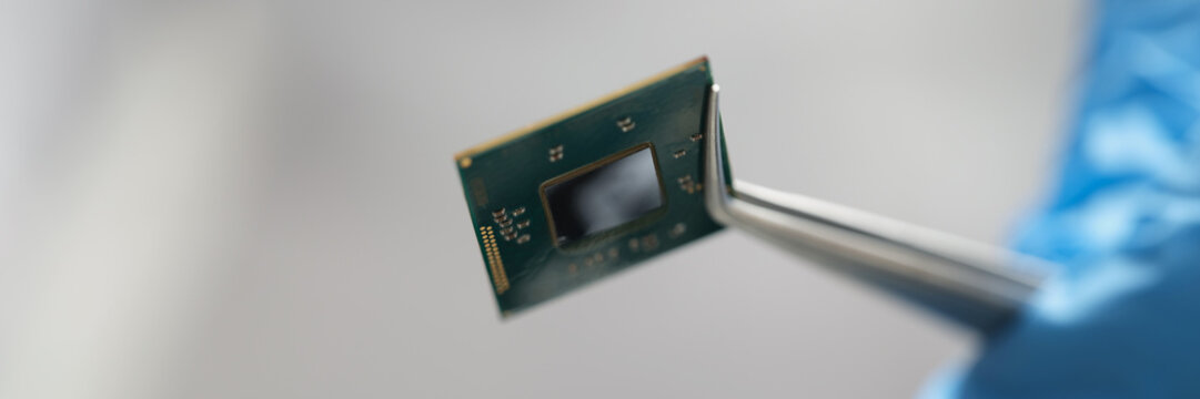 Gloved hands hold a microchip with tweezers, close-up