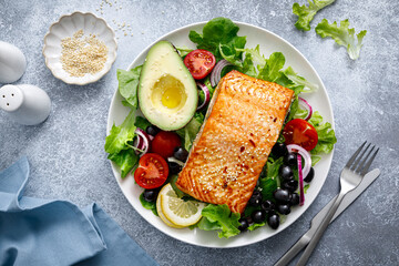 Grilled salmon fish fillet and fresh vegetable salad with tomato, red onion, black olives and avocado