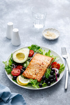 Grilled salmon fish fillet and fresh vegetable salad with tomato, red onion, black olives and avocado
