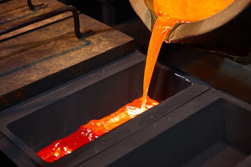 Molten silver is poured from the ladle into a black rectangular graphite mold.