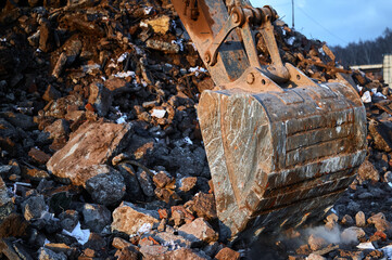 Bucket of excavator digs leftovers of destroyed building