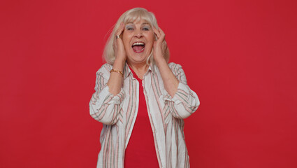 Joyful senior woman laughing out loud after hearing ridiculous anecdote funny joke, feeling carefree amused, positive people lifestyle. Elderly grandmother isolated alone on red studio wall background