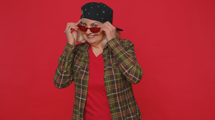 Fototapeta na wymiar Portrait of seductive cheerful stylish elderly woman wearing sunglasses, charming smile. People emotions concept. Senior lovely mature grandmother posing isolated alone on red studio wall background