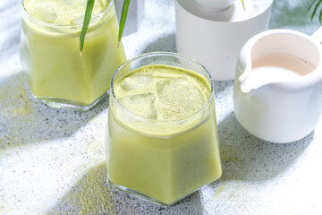 Cold matcha green tea drink. Iced matcha latte cocktail in two glasses with summer tropical palm leaves on white background copy space