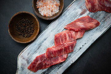 On a vintage wooden cutting board, raw meat, fork, and salt