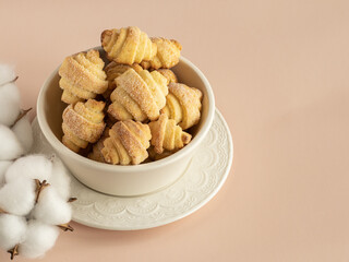 Pastry rolls. Mini cottage cheese croissants, close up. Bagels with sugar in the white ceramic bowl on the white ceramic plate. Сotton flowers. Dusty rose background. Copy space