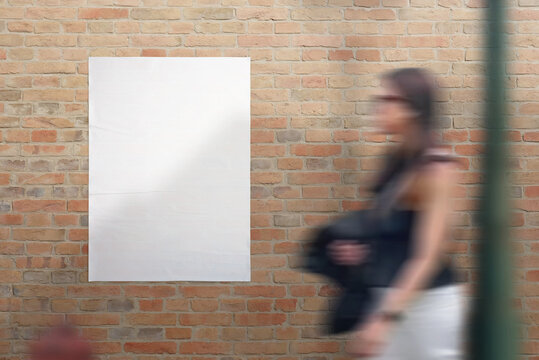 Blank white crumpled poster on street brick wall. Young woman passing