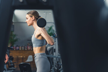 Beautiful girl in gray sportswear doing squats with dumbbells at the gym. High quality photo