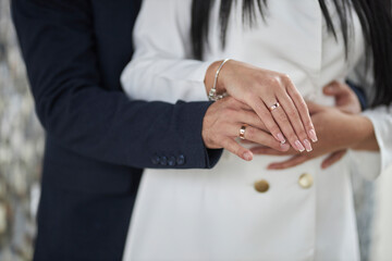 Obraz premium the groom hugs the bride at the wedding, close-up of the hands of the newlyweds. groom in blue jacket hugging bride in white wedding dress