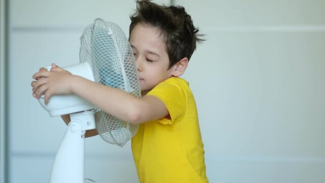 preschool boy cooling in front of fan. Little child refreshing from heat in front of small fan at home. Cute small kid play with ventilator blowing cool wind alone.