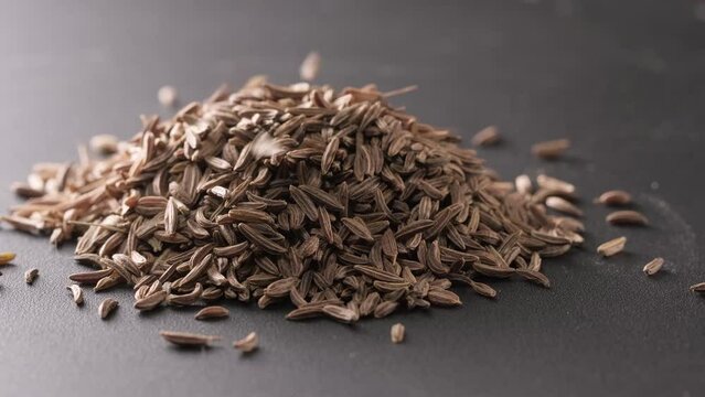 4K. Cumin Seeds rotating on turntable on a slate background. Seasoning cumin or jeera, a lot of seeds rotating. Pouring caraway seeds on a stone table. Spices for cooking food. cooking ingredients