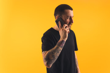 Young man talking on the phone, tattooed arms, looking away studio shot copy space isolated yellow background . High quality photo