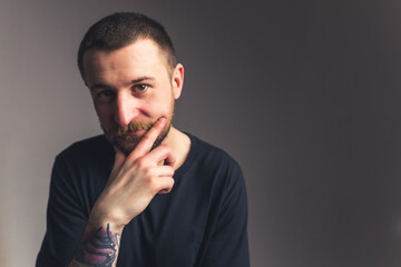 young bearded Caucasian hipster looking at the camera and touching his face, tattooed arm isolated copy space studio shot . High quality photo