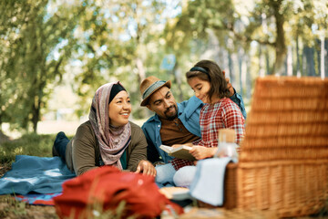 Happy Muslim family reading book on picnic in nature.