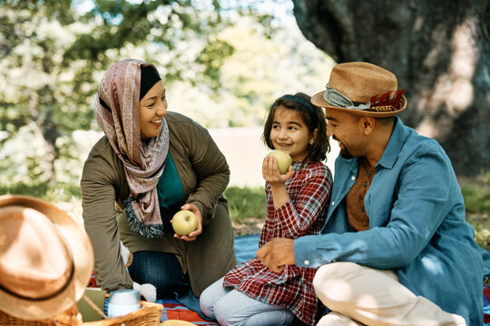 Happy Muslim family eats apples while being on picnic in park.